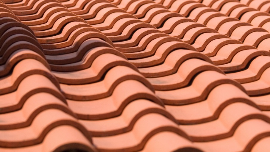 Close-up view of rows of terracotta-colored curved roof tiles, arranged in a repeating wavy pattern—an example often seen in Fullerton for those considering clay vs concrete in professional tile roofing services.
